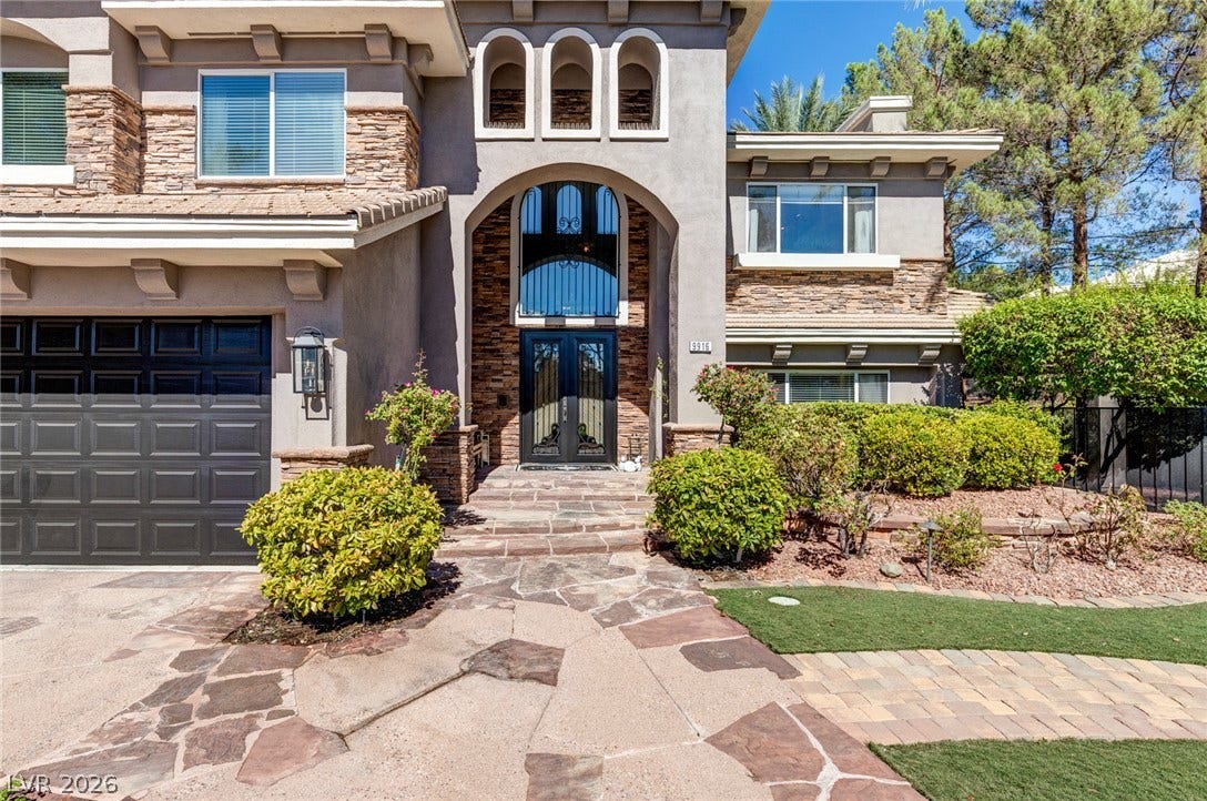 9916 Aspen Knoll Court, Las Vegas, NV 89117 An arched stone entryway leads to grand steel double front doors flanked by manicured landscaping.