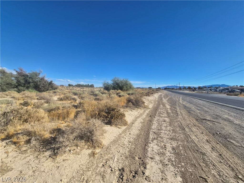 4221 N Leslie Street, Pahrump, NV 89060 Desert brush frames a wide property line along a paved roadway under blue skies.
