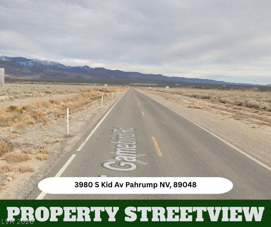 A paved road stretches toward majestic distant mountains under a dramatic desert sky.