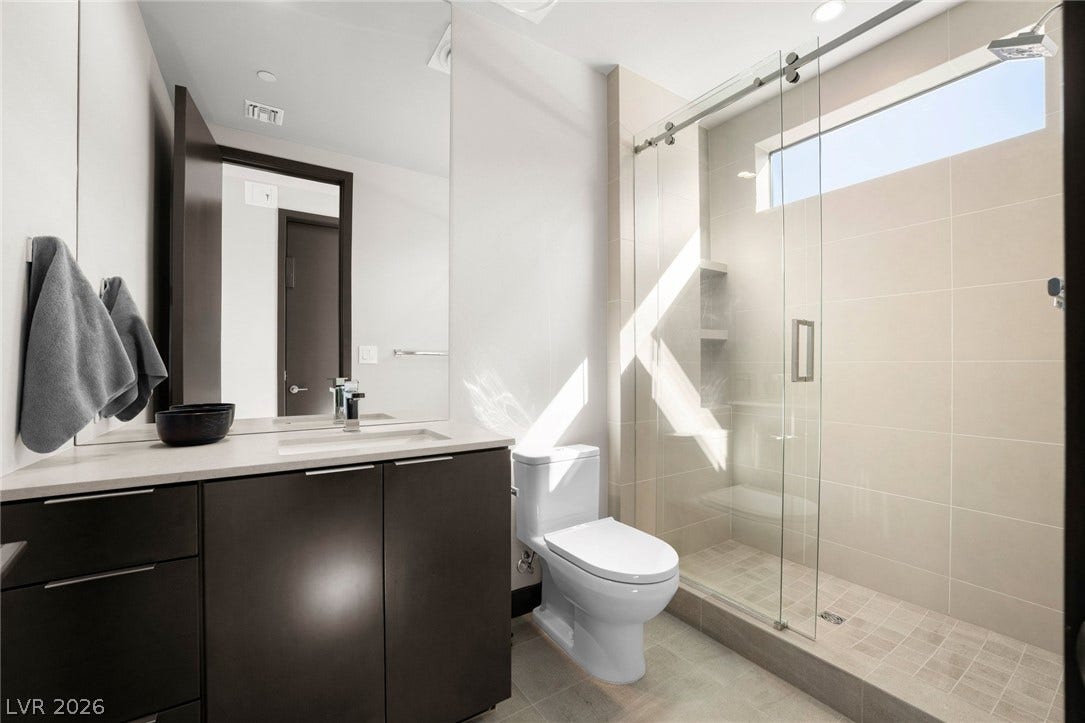 34 Lakefront Drive, Henderson, NV 89011 A contemporary bathroom features a glass-enclosed shower, stone counters, and elegant tile flooring.