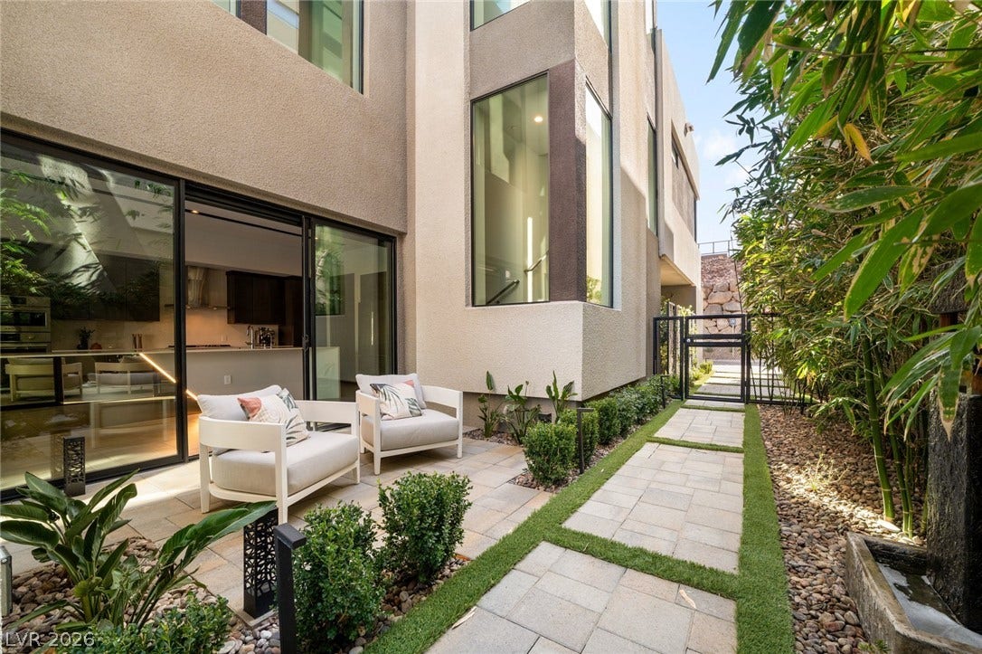 34 Lakefront Drive, Henderson, NV 89011 A secluded stone patio features a stone pathway bordered by lush greenery and modern stucco architecture.