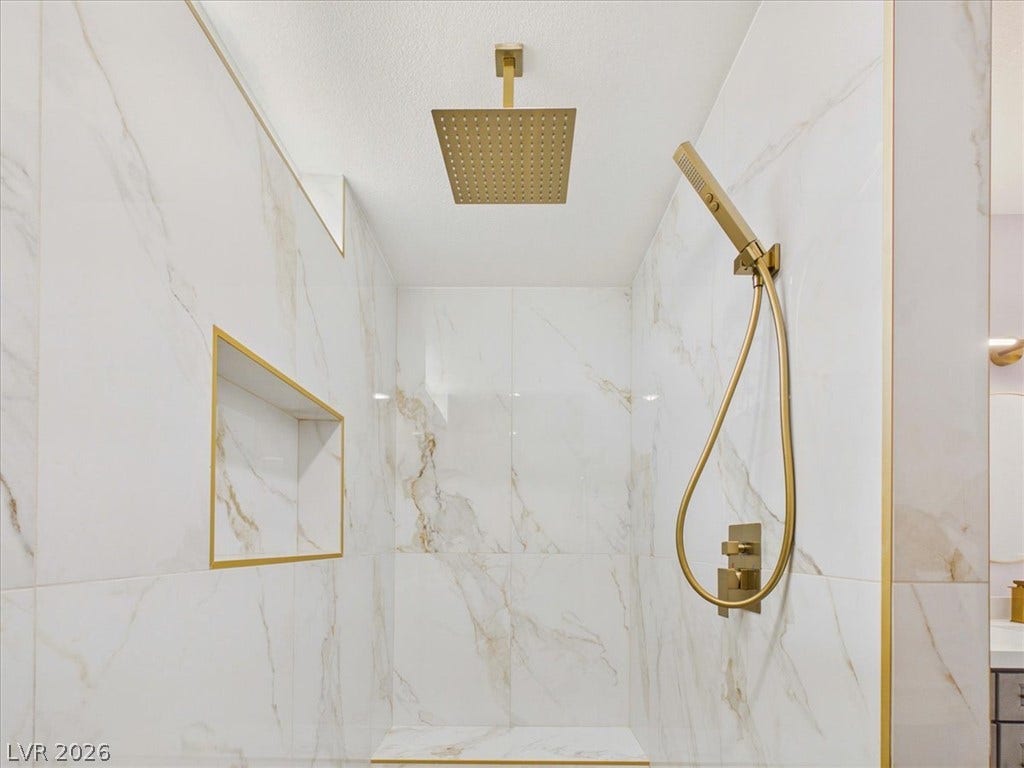 6680 S Raintree Court, Pahrump, NV 89061 Elegant gold fixtures accent the marble-tiled walls of this luxurious walk-in shower.