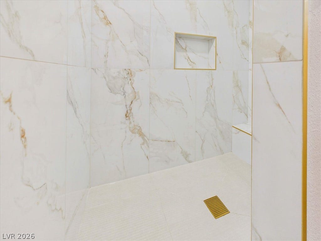 6680 S Raintree Court, Pahrump, NV 89061 Floor-to-ceiling marble-look tile walls highlight a modern walk-in shower with gold-toned trim and fixtures.