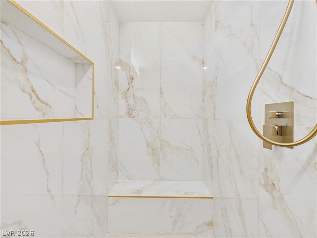 6680 S Raintree Court, Pahrump, NV 89061 Elegant marble tile surrounds this walk-in shower featuring a built-in bench and brass fixtures.