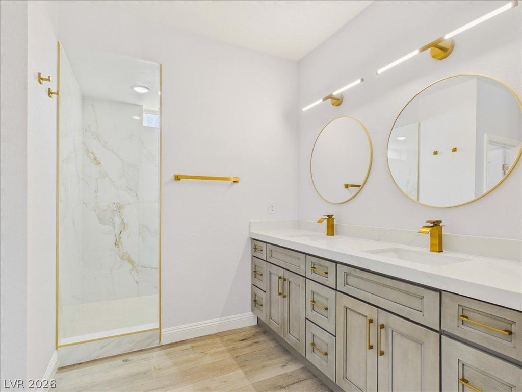 6680 S Raintree Court, Pahrump, NV 89061 Gleaming gold fixtures elevate this modern bathroom featuring a double vanity and walk-in shower.