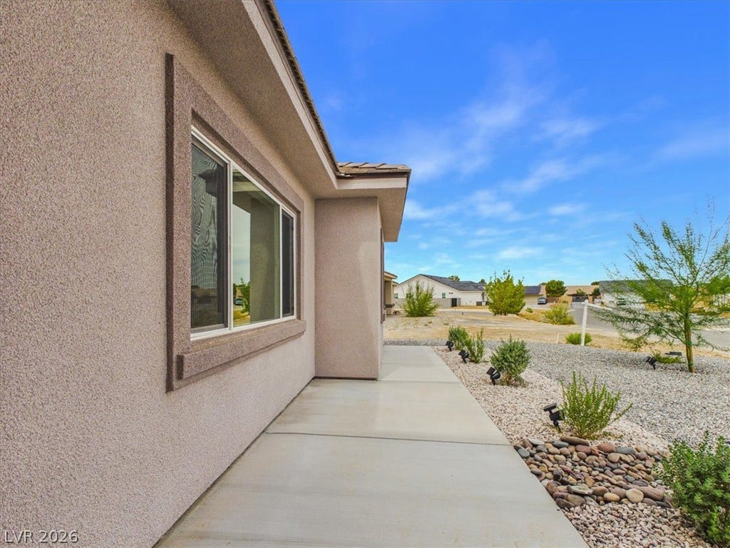 6680 S Raintree Court, Pahrump, NV 89061 Smooth concrete paths border low-maintenance desert landscaping alongside the stucco exterior under bright blue skies.