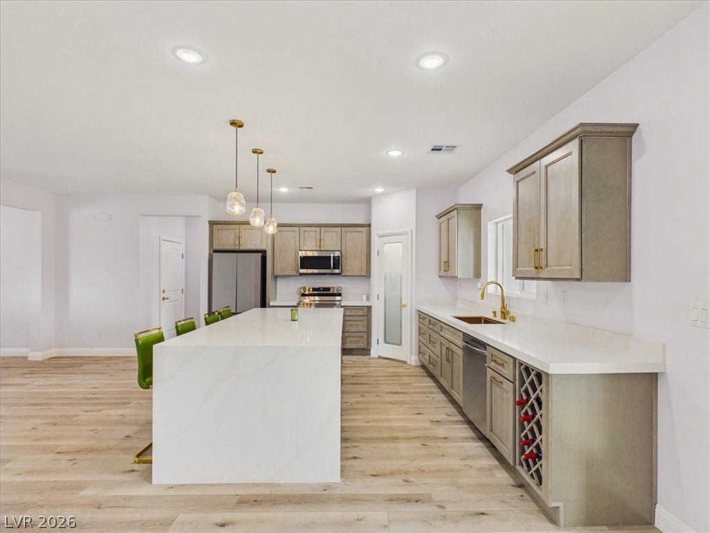 6680 S Raintree Court, Pahrump, NV 89061 An expansive waterfall island anchoring a light-filled gourmet kitchen with warm wood-grained flooring.