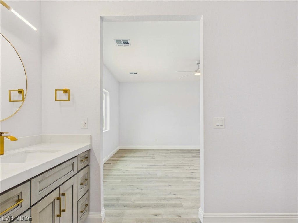 6680 S Raintree Court, Pahrump, NV 89061 An open doorway connects the sleek vanity area to a bright adjoining bedroom with wood-style flooring.