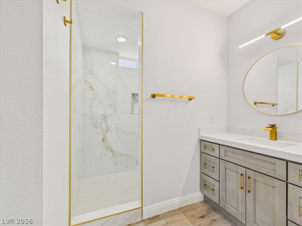 6680 S Raintree Court, Pahrump, NV 89061 Elegant gold hardware accents complement the marble shower and modern vanity of this bathroom.