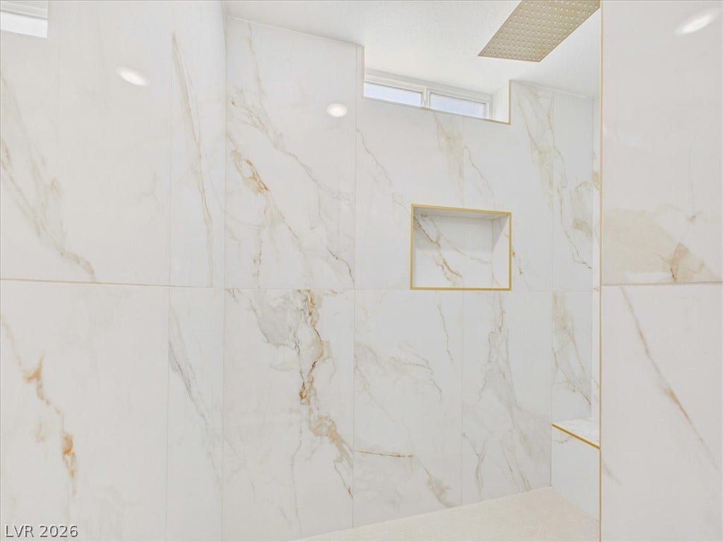 6680 S Raintree Court, Pahrump, NV 89061 Gleaming marble-patterned tile walls and elegant gold accents line this modern walk-in shower.