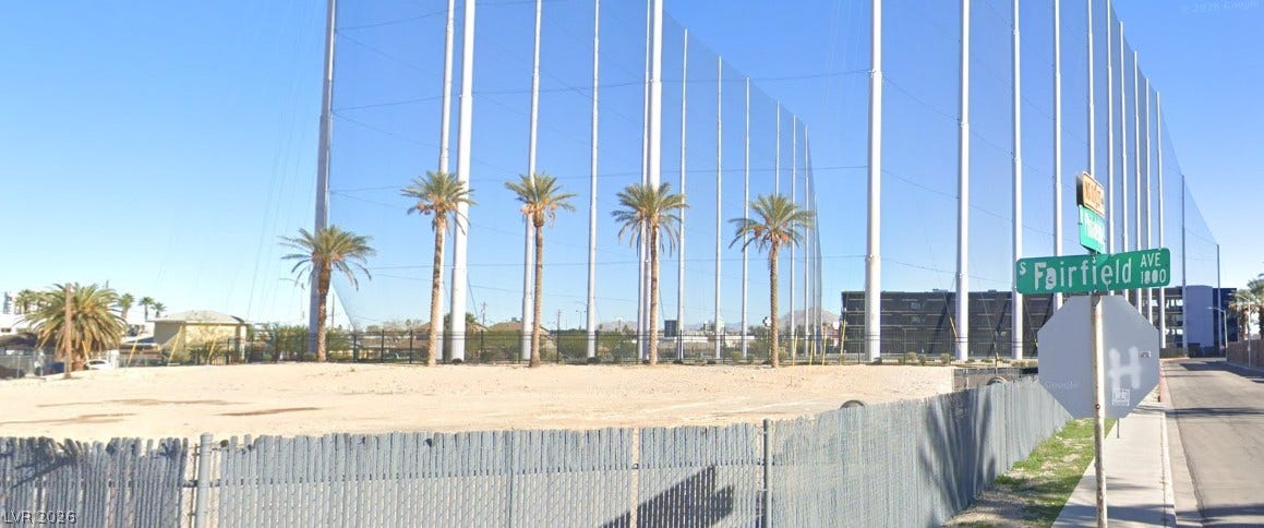 Palm trees stand tall against a clear blue sky bordering an open lot.