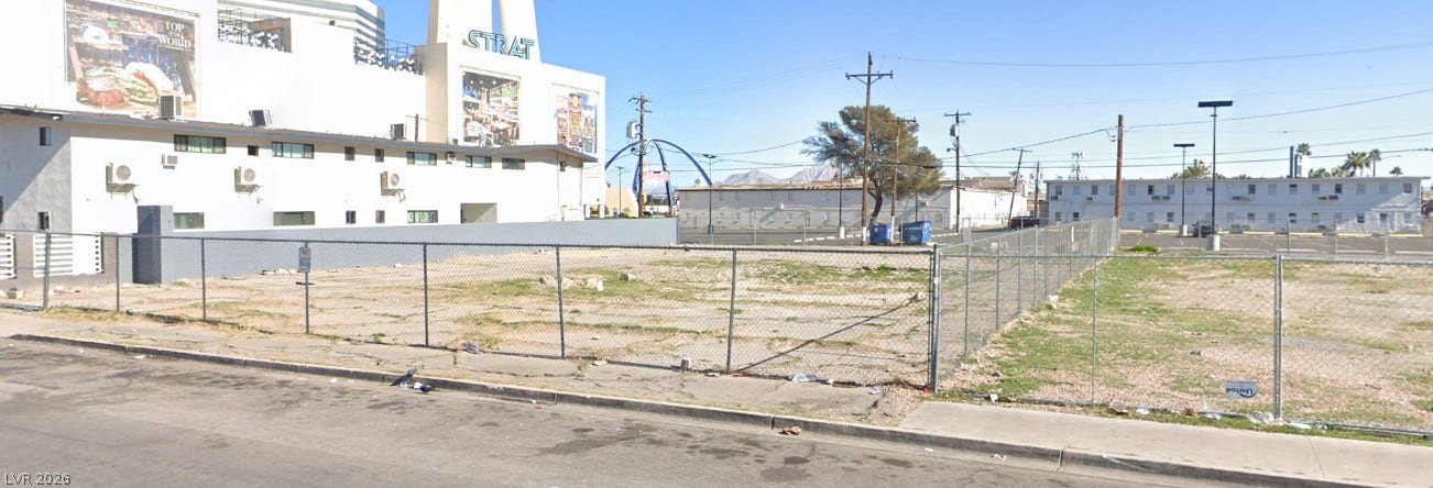 A spacious, level vacant lot sits secured by chain-link fencing near neighboring structures.