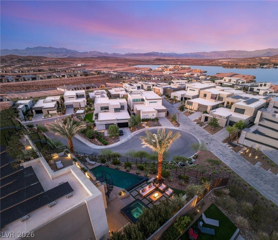 An aerial perspective reveals a modern neighborhood nestled against a tranquil lake and distant mountains at dusk.