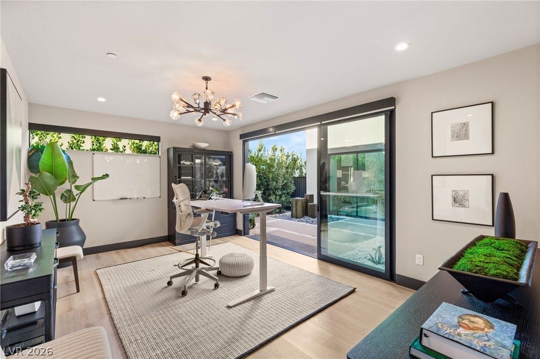 An inviting office space with a contemporary chandelier offers seamless access to a private outdoor oasis through sliding glass doors.