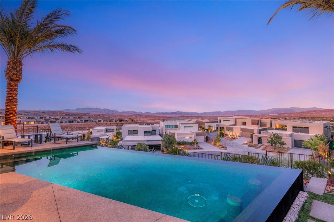 An inviting infinity pool overlooks a vibrant desert landscape with distant mountains at dusk.