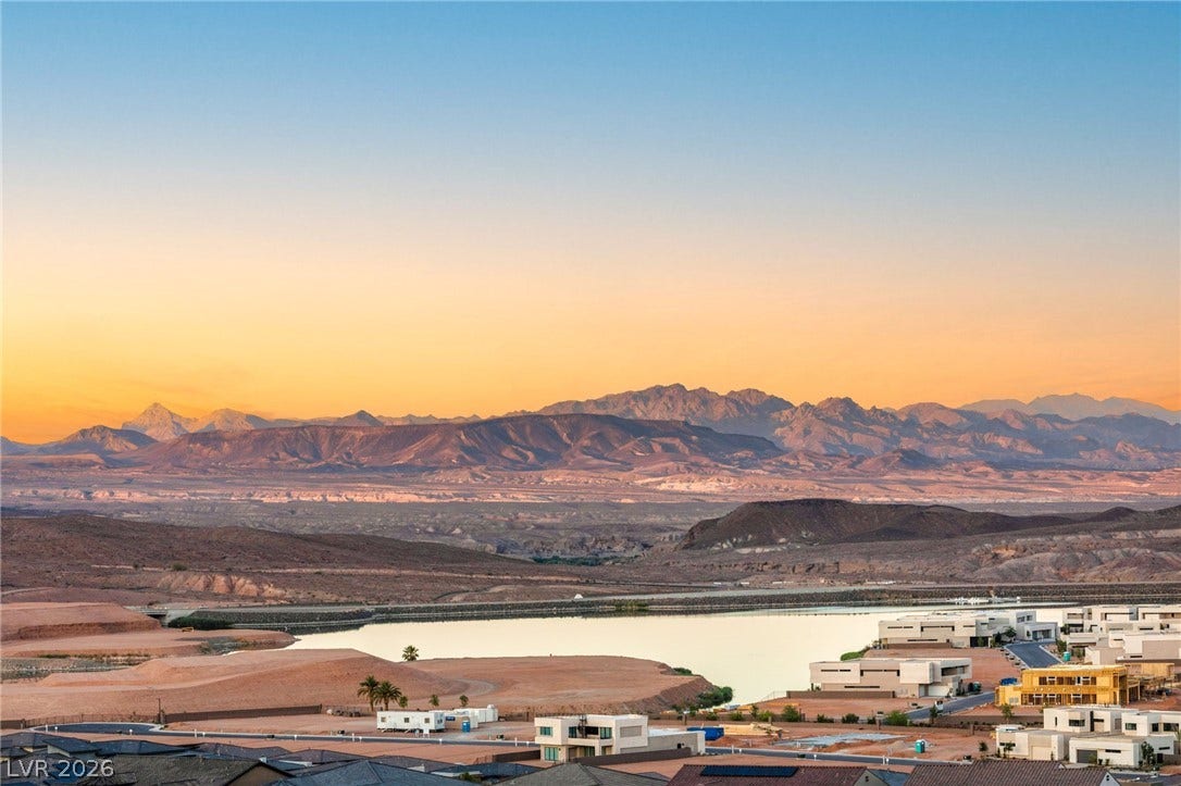 Golden hour illuminates a desert landscape featuring a tranquil lake, mountain range, and contemporary residences.