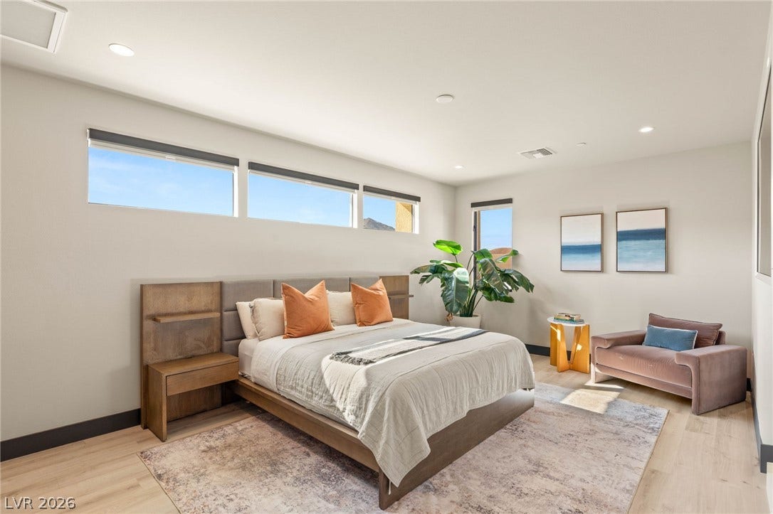 Recessed lighting illuminates this inviting bedroom, featuring light wood flooring and well-lit windows.
