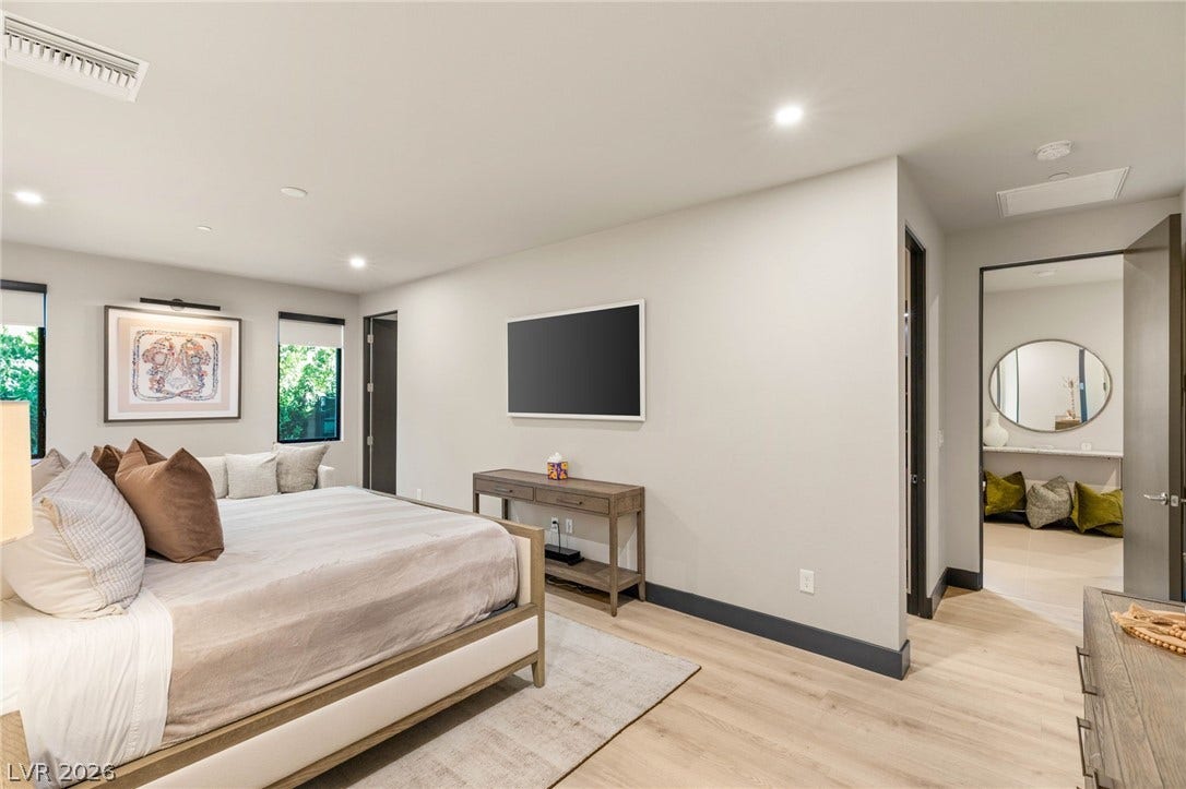 Recessed lighting illuminates the spacious bedroom with light wood flooring, offering a seamless transition to the adjacent bathroom.