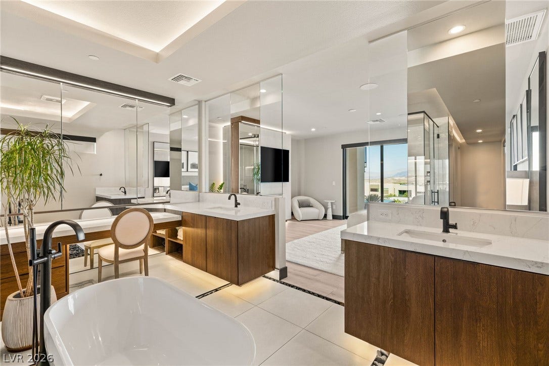 Luxurious primary bath with dual vanities, soaking tub, and a mountain view through the glass sliding doors.