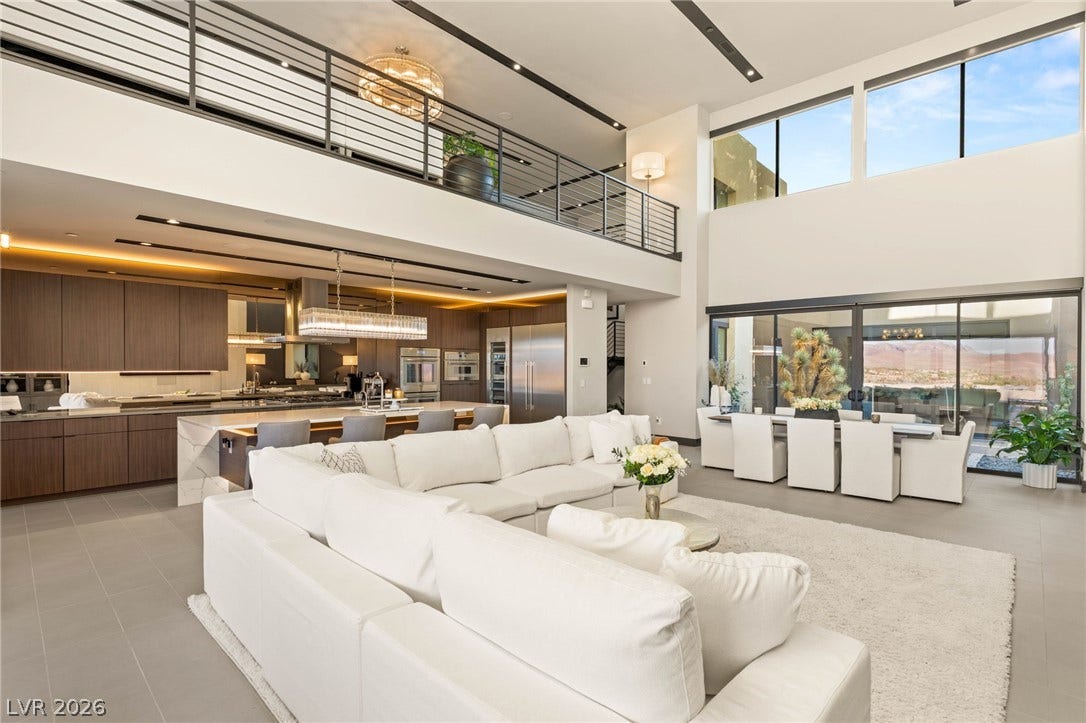 An open floorplan seamlessly connects the living room, dining area, and kitchen, all beneath high ceilings with a second-story walkway.