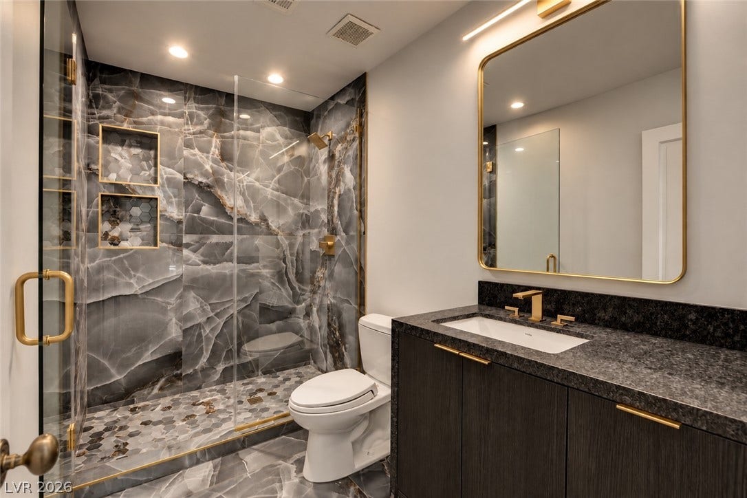 2001 Silver Avenue, Las Vegas, NV 89102 Richly veined stone tiles enclose a modern walk-in shower alongside a dark stone-topped vanity.