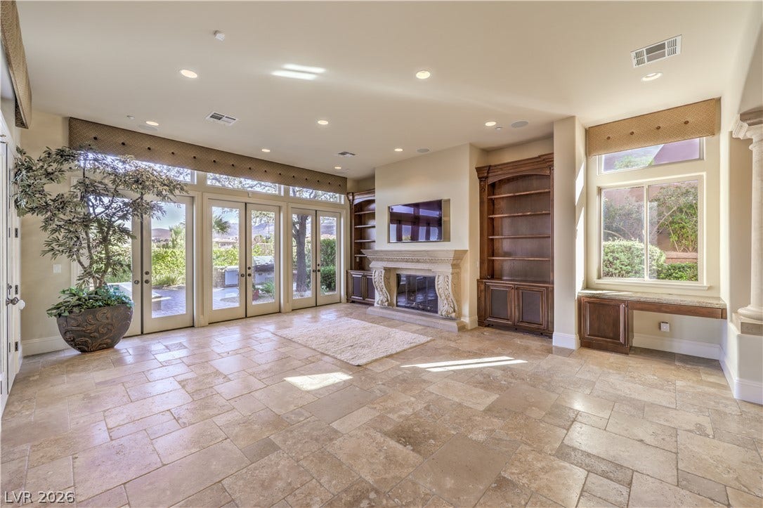 16 Anthem Pointe Court, Henderson, NV 89052 French doors and polished tile flooring frame a stately stone fireplace with custom built-in cabinetry.