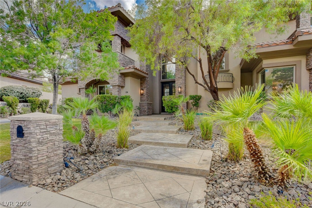 84 Kittansett Loop, Henderson, NV 89052 A patterned concrete walkway leads past desert landscaping to a stone-accented entryway.