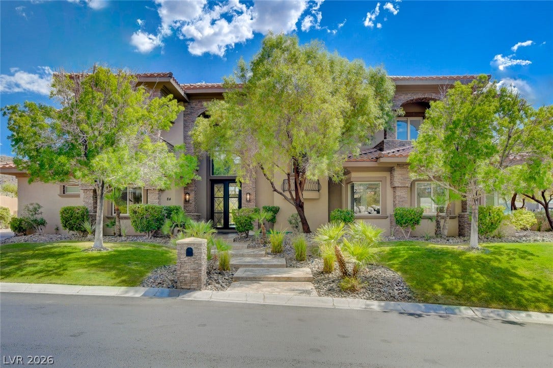 84 Kittansett Loop, Henderson, NV 89052 Mature trees and neat stone accents frame a welcoming double-door entrance under sunny skies.