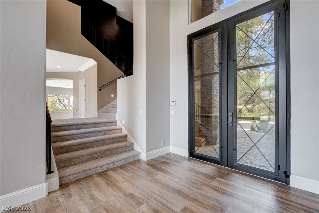 84 Kittansett Loop, Henderson, NV 89052 Double glass doors open into a towering foyer featuring wood-look tile floors and carpeted stairs.