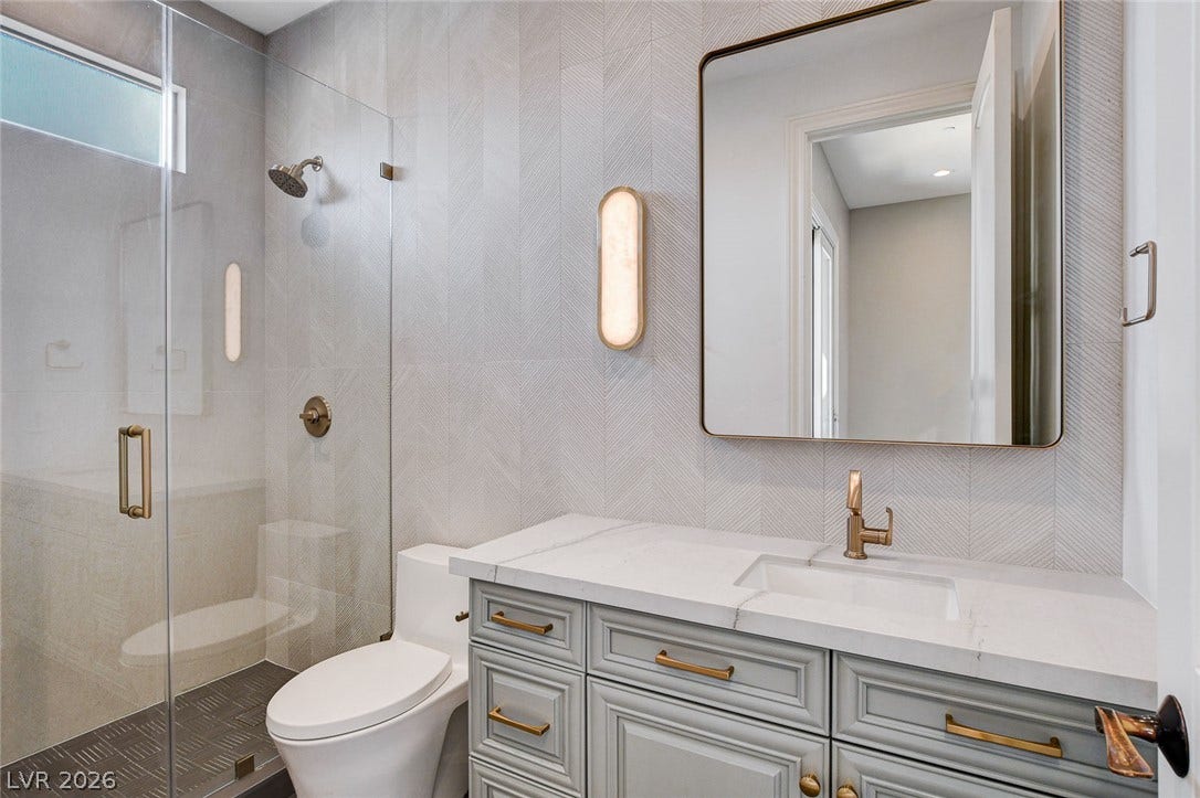 84 Kittansett Loop, Henderson, NV 89052 Elegant textured wall tiling and custom cabinetry define this modern bathroom space.