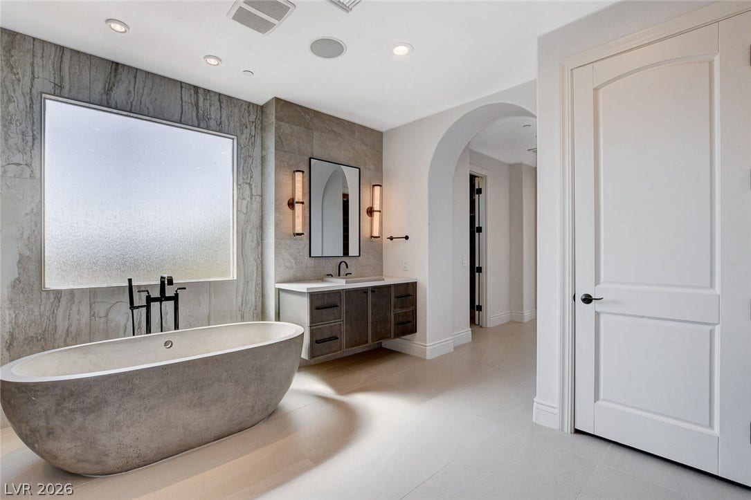 84 Kittansett Loop, Henderson, NV 89052 A freestanding tub rests beside large windows under high ceilings in this bathroom.