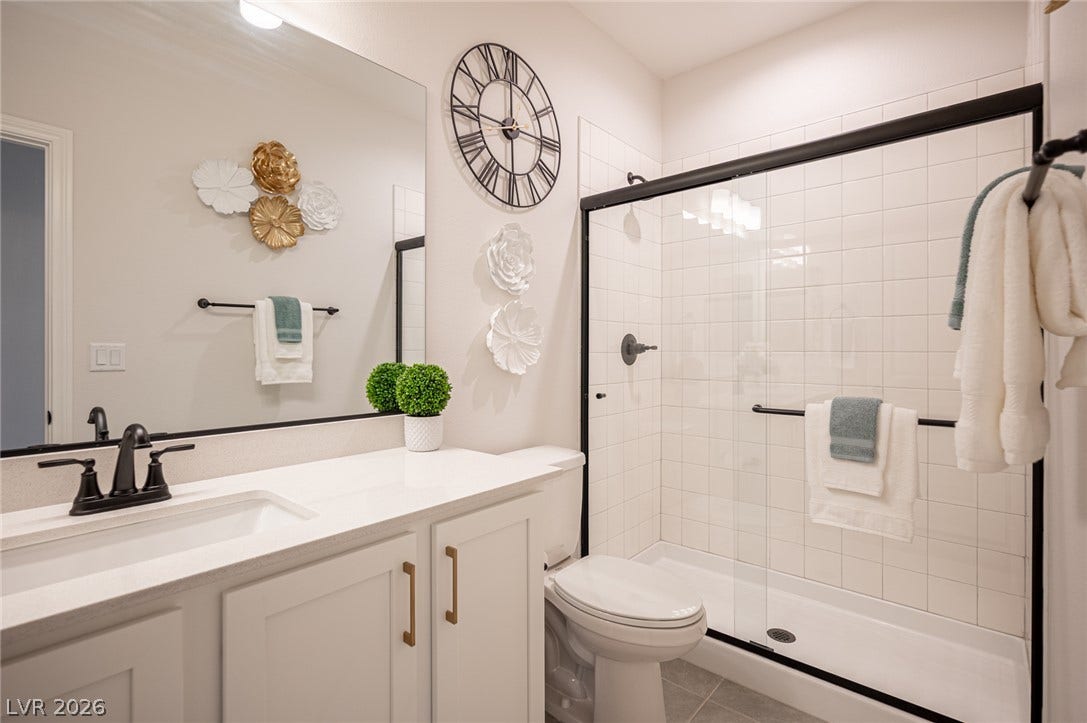 320 Della Pergola Place, Henderson, NV 89015 A modern vanity with stone counters complements a tiled walk-in shower with black-framed glass doors.