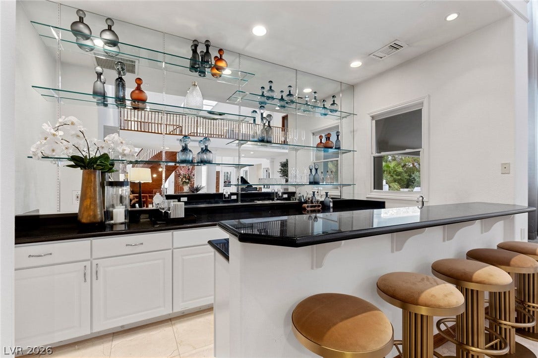 Granite counters and custom glass shelving elevate this home bar area.