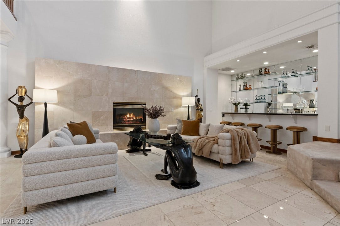 A grand stone fireplace and adjacent wet bar define this elegant living area.