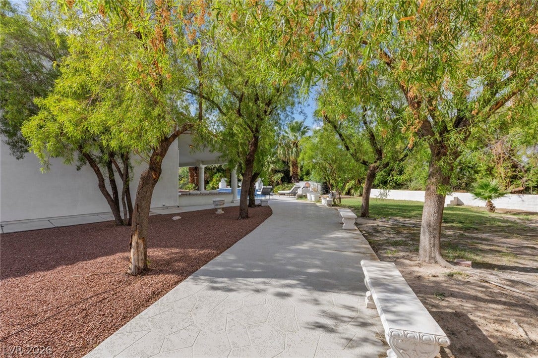 Mature trees shade a paved stone path leading through the landscaped grounds.