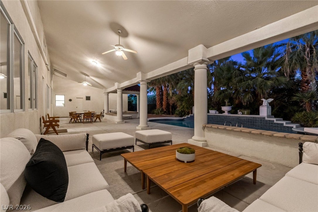 A spacious covered patio overlooks the sparkling pool area framed by classic columns.