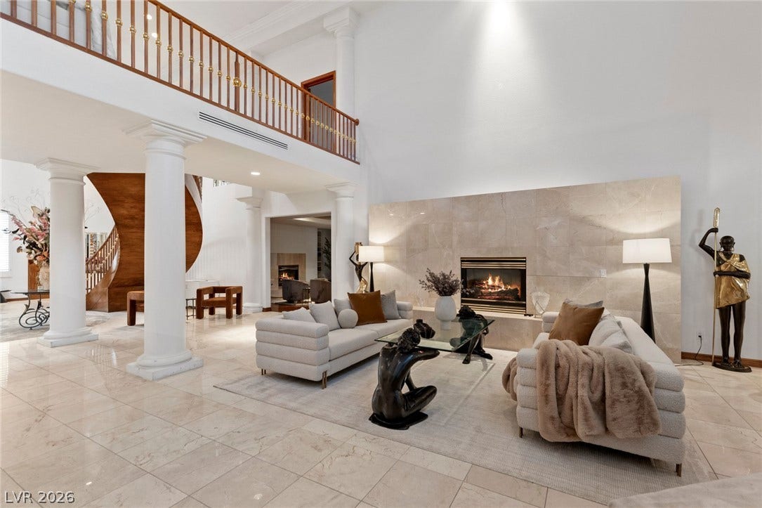 Polished tile floors and soaring ceilings frame a grand stone fireplace in this elegant space.