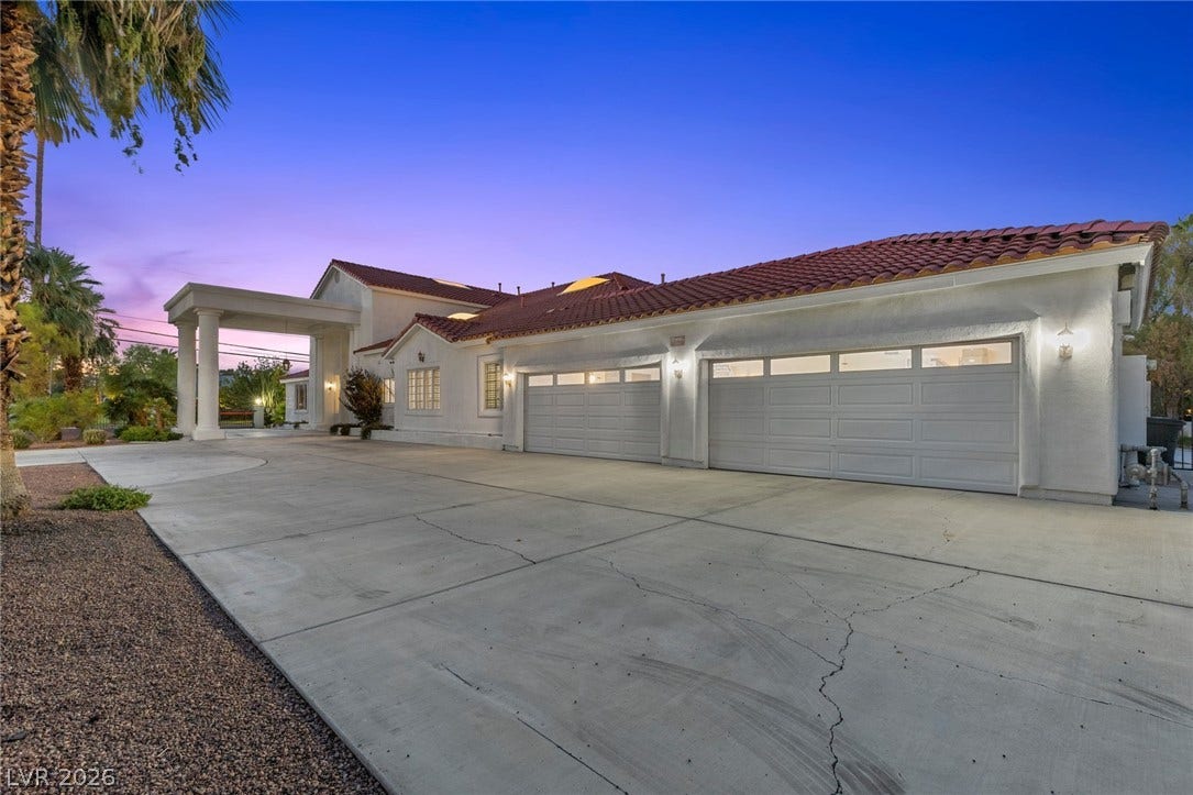 A spacious concrete driveway leads toward multi-car garages under a classic tile roof.
