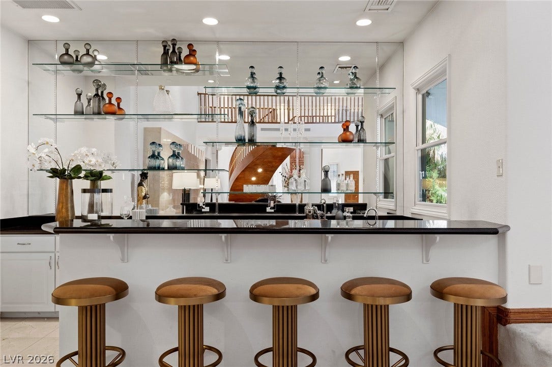 Mirrored walls and custom glass shelving elevate this sleek entertainment bar with dark stone counters.