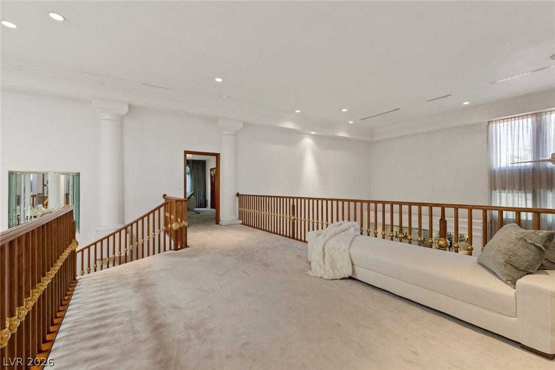 An open upper landing showcases classic columns and a wooden balustrade over plush carpeting.