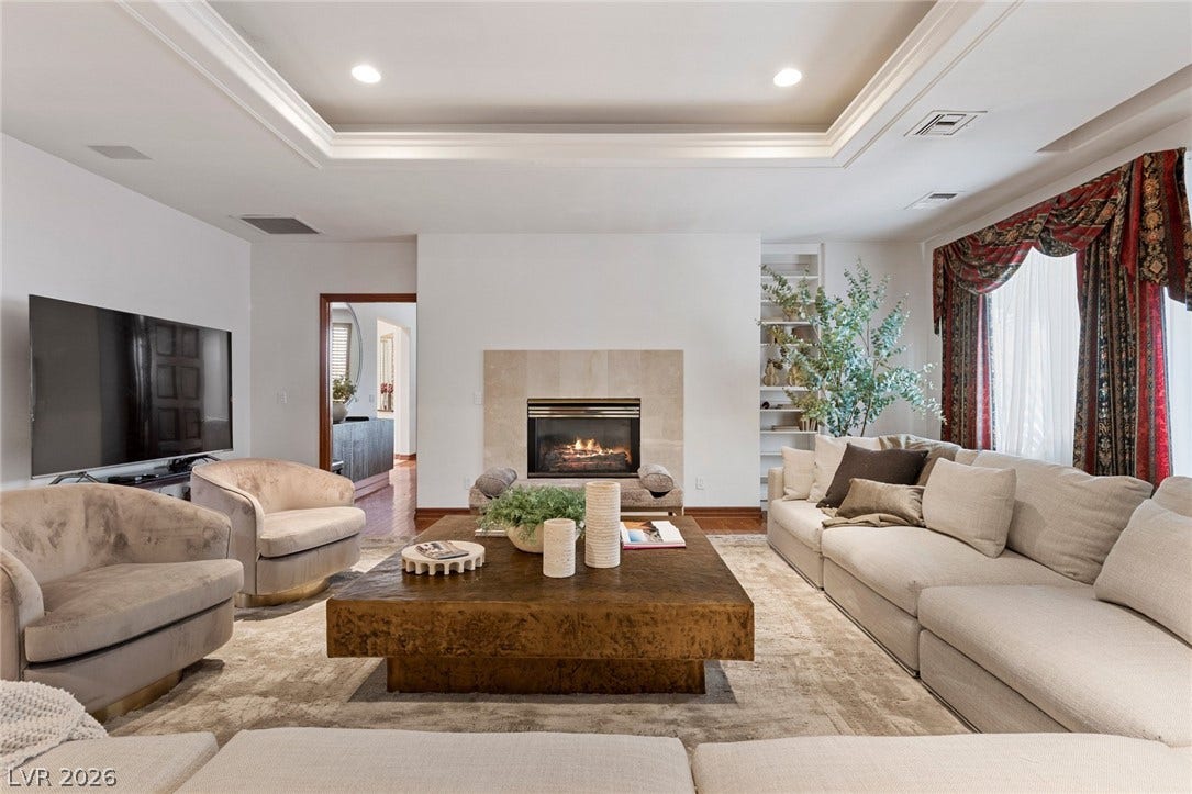 An elegant tray ceiling and central fireplace anchor this inviting living space.