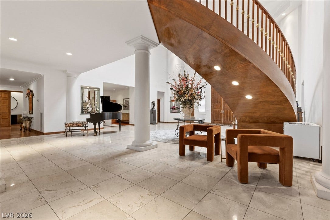 A grand curved staircase rises from the polished tile floors of this expansive entryway.