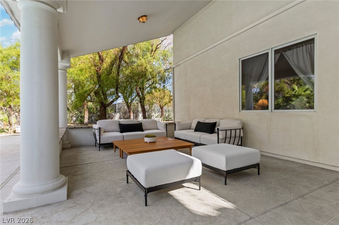Shaded concrete patio features classic supportive columns and views of the surrounding mature trees.