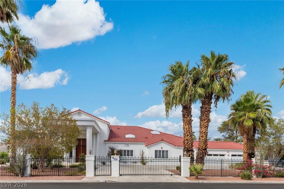 Palm trees flank the secure gated entry of this classic stucco home with tiled roof.