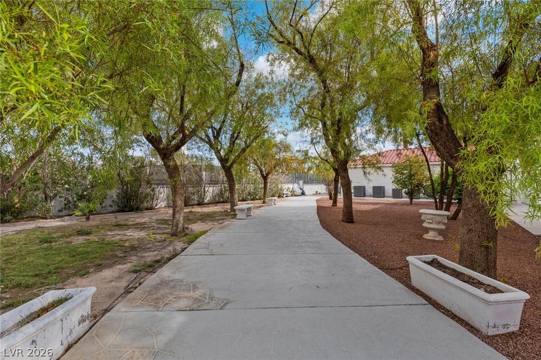 Mature trees shade a paved concrete pathway winding through the spacious rear grounds.