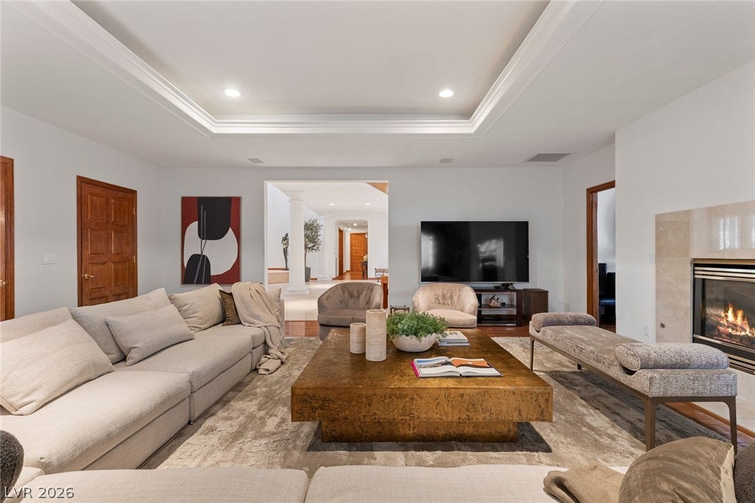 A comforting fireplace warms this spacious living area beneath a classic tray ceiling.