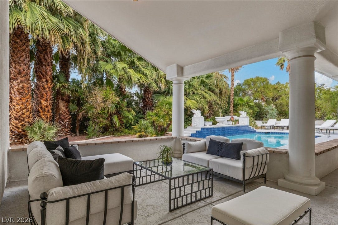 An inviting covered patio features grand supporting columns and overlooks a sparkling swimming pool.