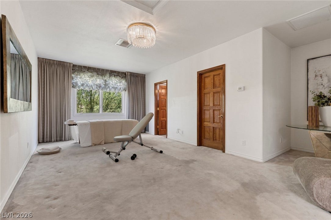 An upstairs bedroom staged as a spacious wellness center featuring soft carpeting and elegant overhead lighting.