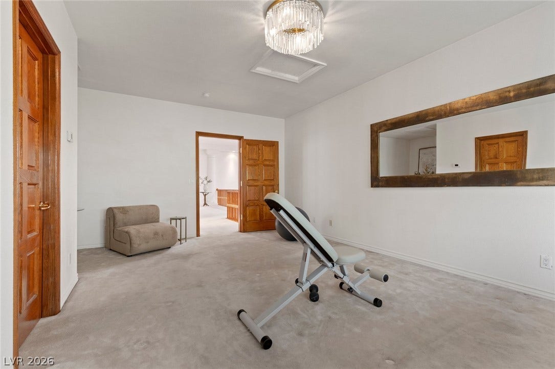 An upstairs  bedroom staged as a spacious wellness center featuring soft carpeting and elegant overhead lighting.