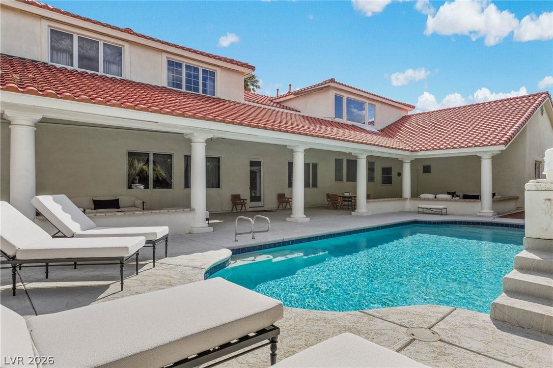 A sparkling swimming pool sits adjacent to a spacious covered patio beneath Spanish tile roofing.